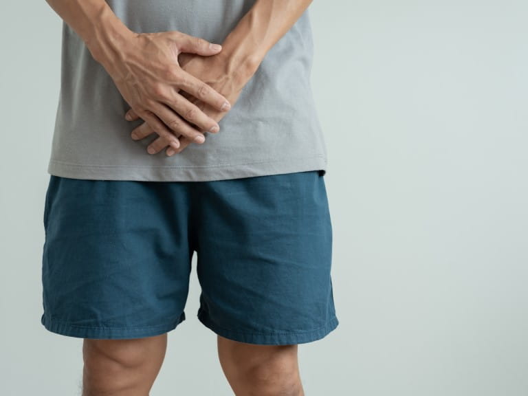 A man ina  grey top and blue shorts holds his stomach in discomfort