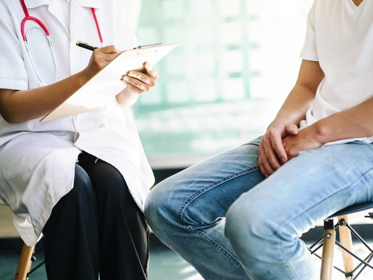 A female doctor sits and discusses with a man whilst making notes on a clipboard