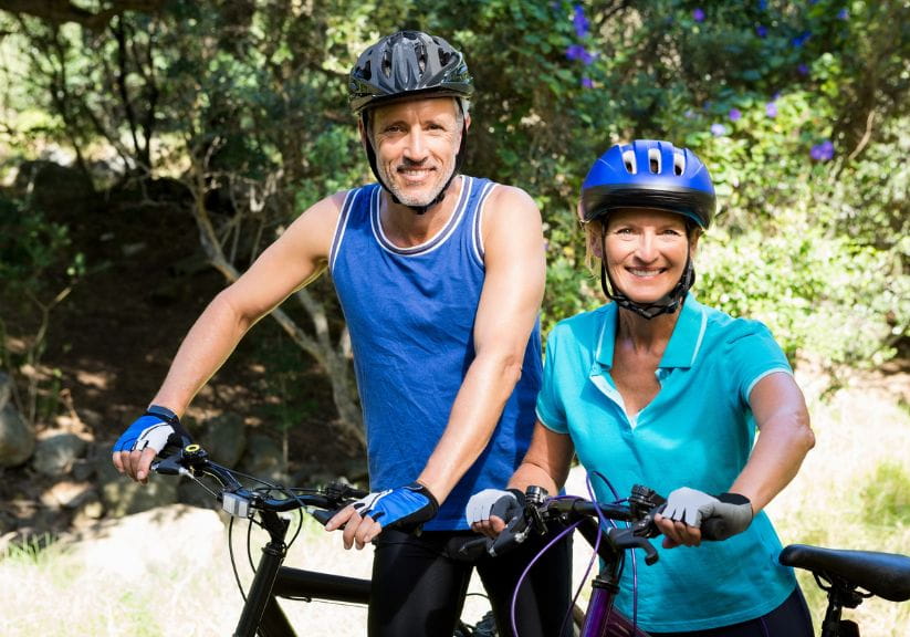 A man and a woman wearing bike helmets standing with their cycles in woodland