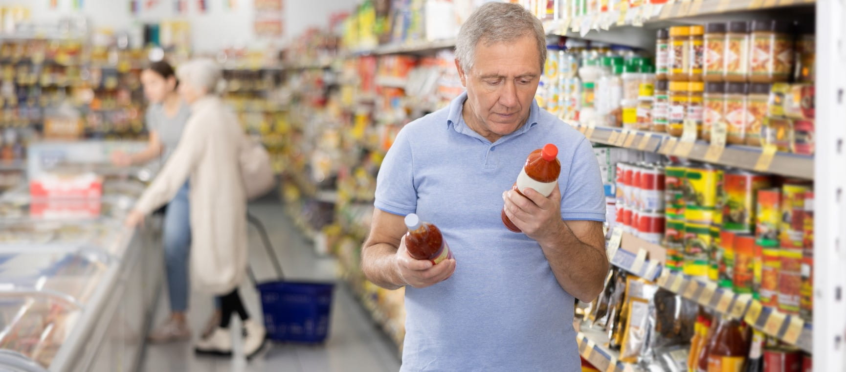 A man reading labels on bottles with sauces in supermarket, carefully examining calorie counts | Getty/JackF