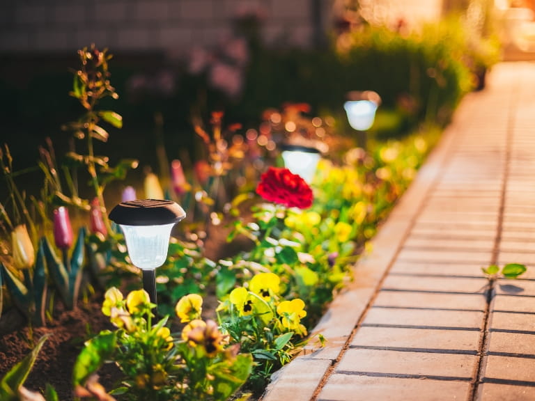 Solar-powered lights illuminating a flower border beside a bricked garden pathway