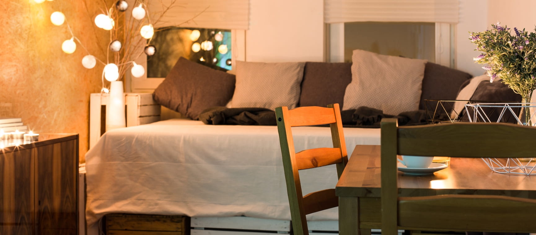 A box room with a single bed covered in cushions, desk and fairy lights