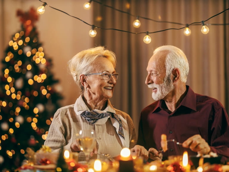 A senior couple enjoying a candle-lit Christmas dinner together with a Christmas tree in the background