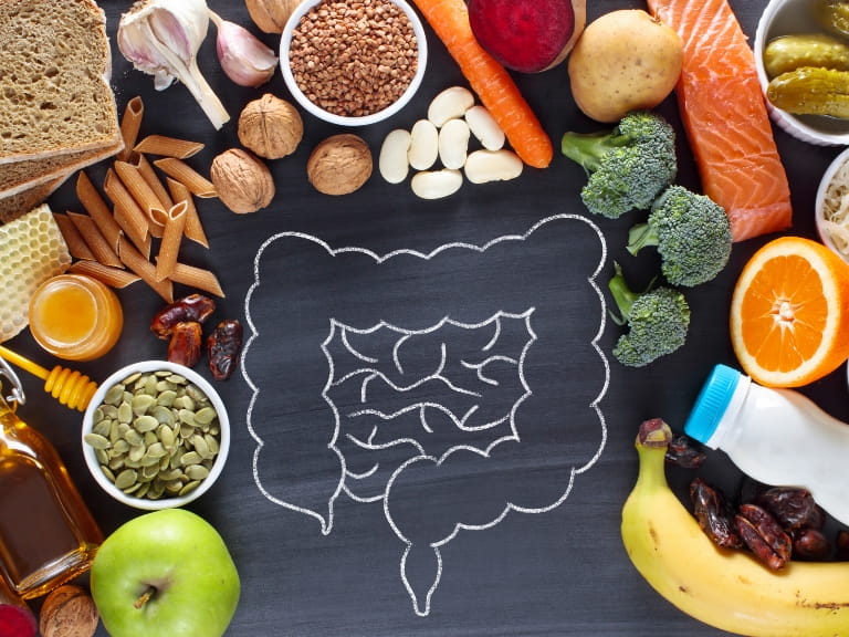 An assortment of gut-friendly foods surrounding a chalk drawing of the intestine, including fruits, vegetables, nuts, fish, pasta and whole grains