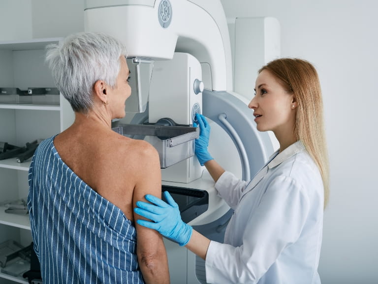 A young female doctor performing a mammogram on an older woman with cropped hair in a hospital environment