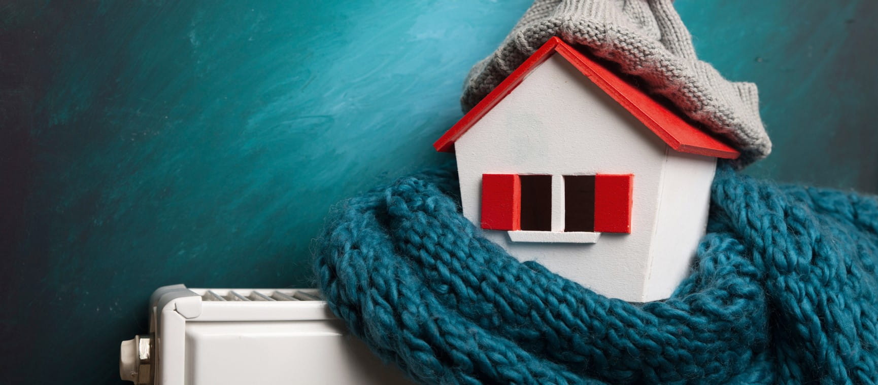 A model of a house on a radiator wearing a scarf to represent winter fuel payments | Shutterstock