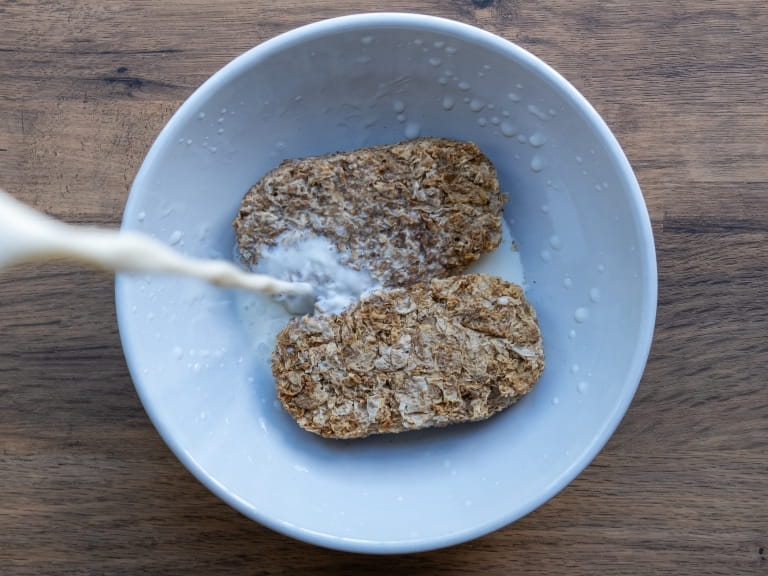Milk being poured over two Weetabix bars in a white bowl
