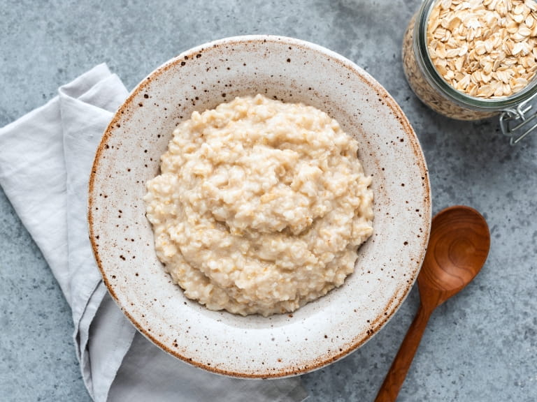 A bowl of porridge with a white napkin and wooden spoon next to a jar of oats