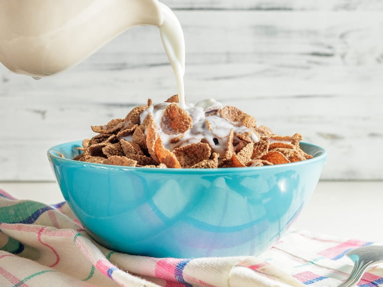 Milk being poured into a blue bowl of bran flakes