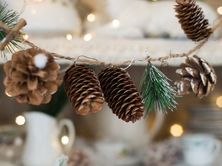 Pine cones, foliage and Christmas lights tied to string to create a natural garland