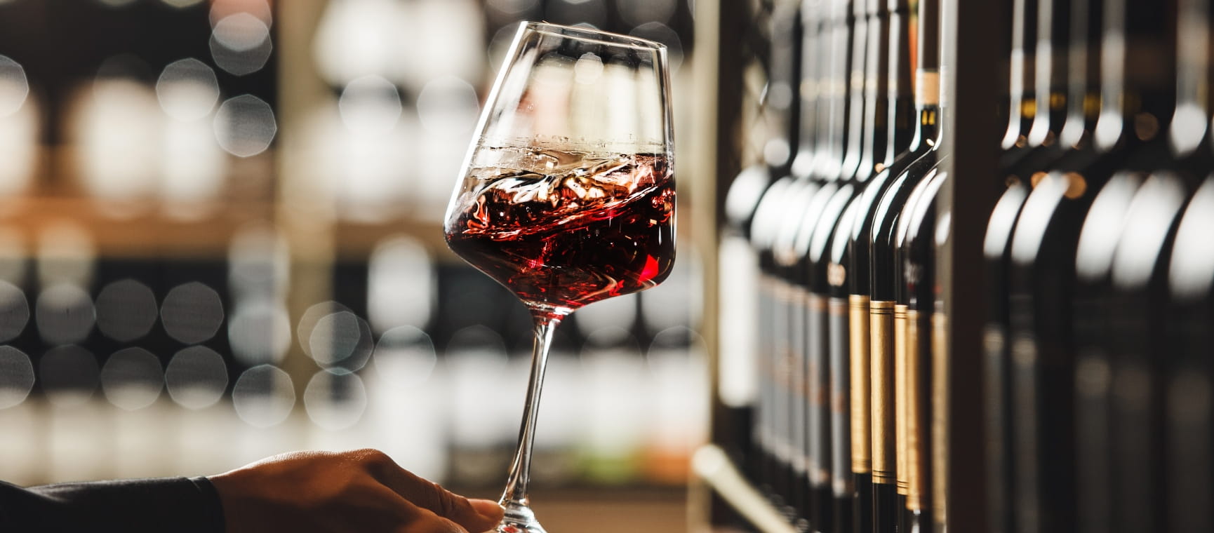 Hand swirling a glass of red wine on a blurred background of a wine cellar