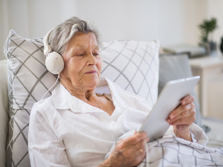 An older woman in bed listening to music through headphones