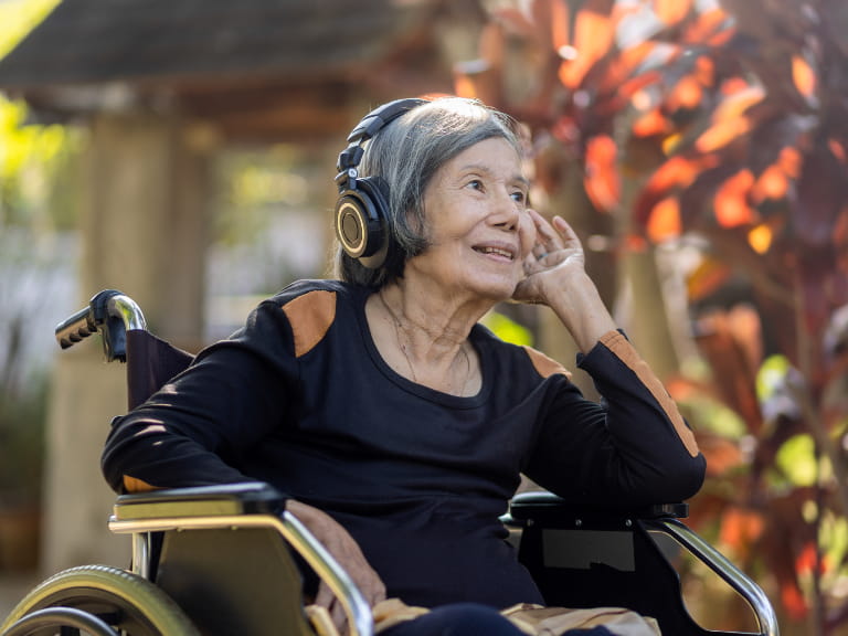 A senior woman in a wheelchair listening to music through headphones outdoors