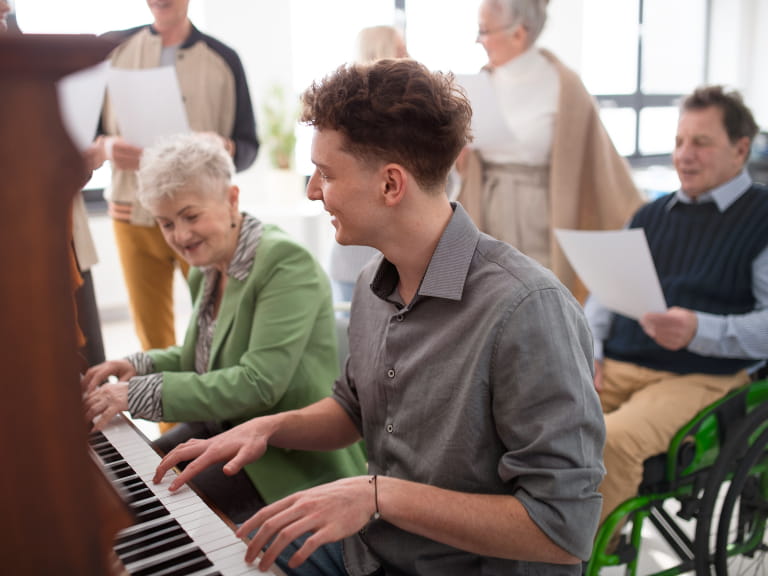 A young man and senior woman play piano for a choir