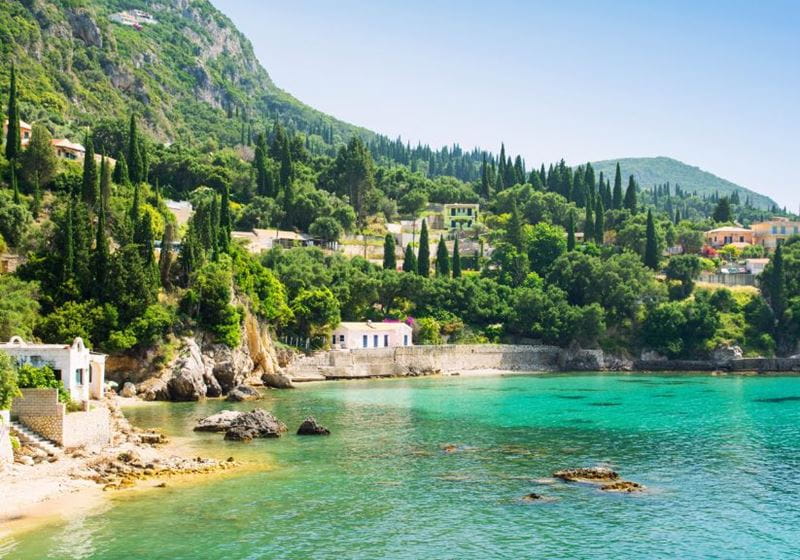 a cove in Corfu with a sandy beach and turquoise sea with green hills behind in the sunshine