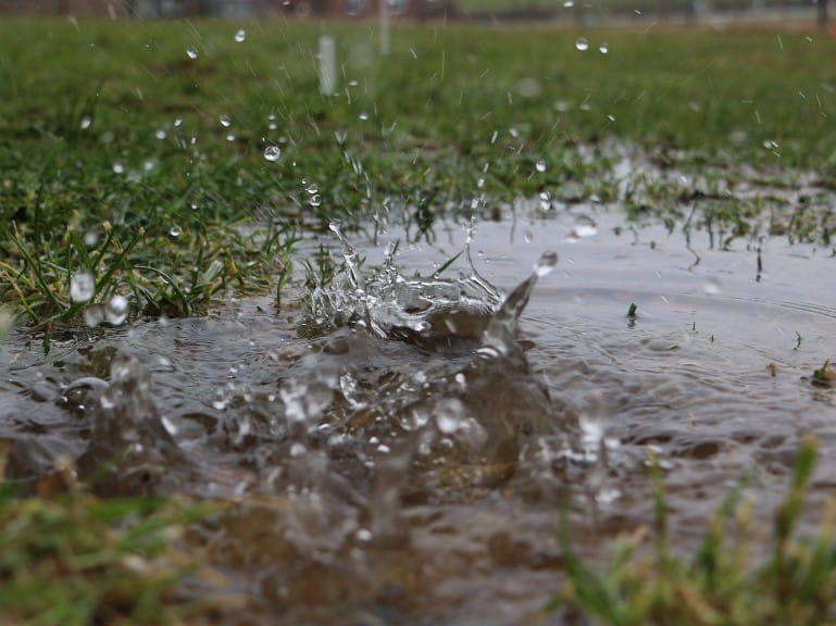 Rain falling on a puddle on a waterlogged lawn | Getty/BiancaGrueneberg