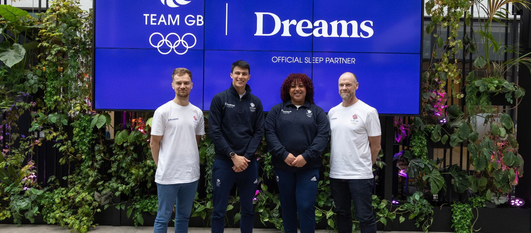 Two Olympic team members and two members of the coaching staff in front of the Dreams logo
