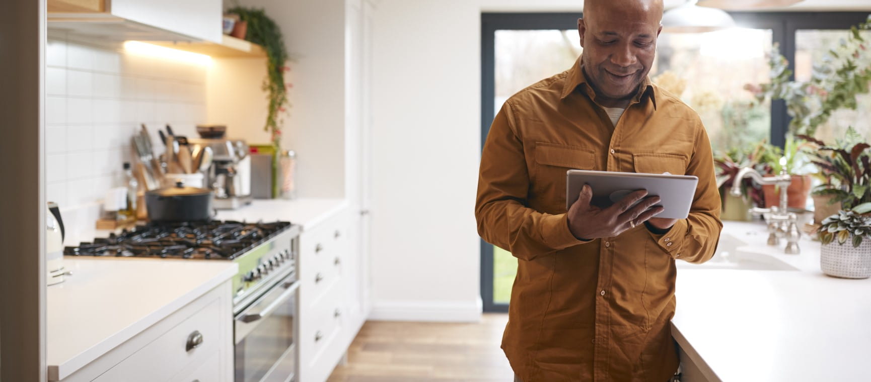 An older man in a kitchen browsing a tablet | Getty/monkeybusinessimages