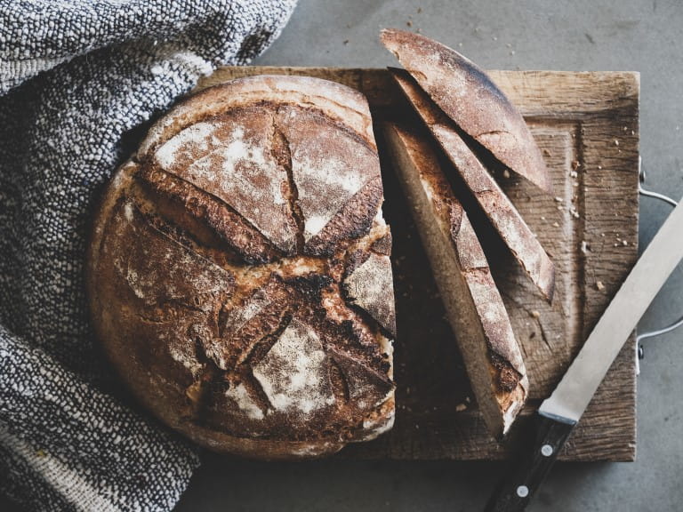 A loaf of bread on a wooden cutting board, half sliced | Picture Pantry