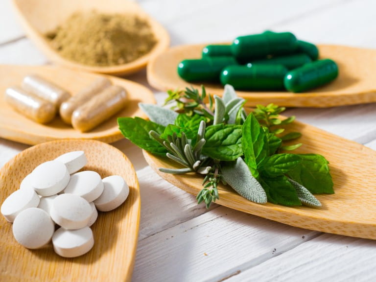 herbal leaves, ground herb powder and medicament pills on bamboo spoons, white wooden table | Getty/S847
