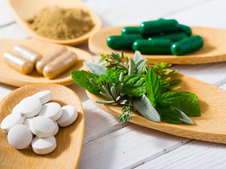 herbal leaves, ground herb powder and medicament pills on bamboo spoons, white wooden table | Getty/S847