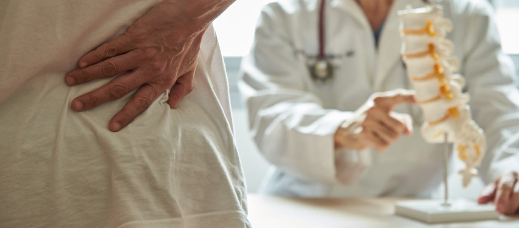 A male doctor explaining lumbar anatomy to female patient complaining of back pain at medical clinic | Getty