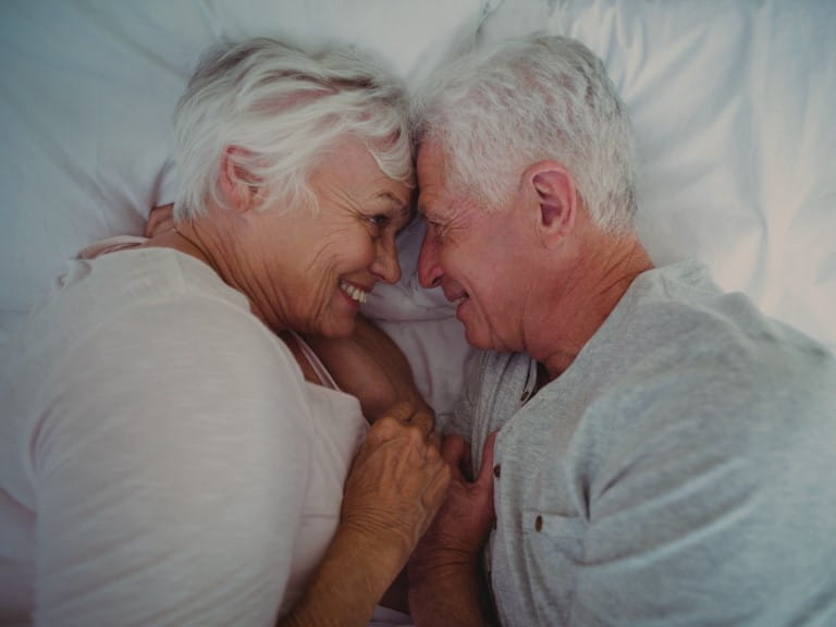 High angle view of senior couple touching head while lying on bed in room | Getty/Wavebreakmedia