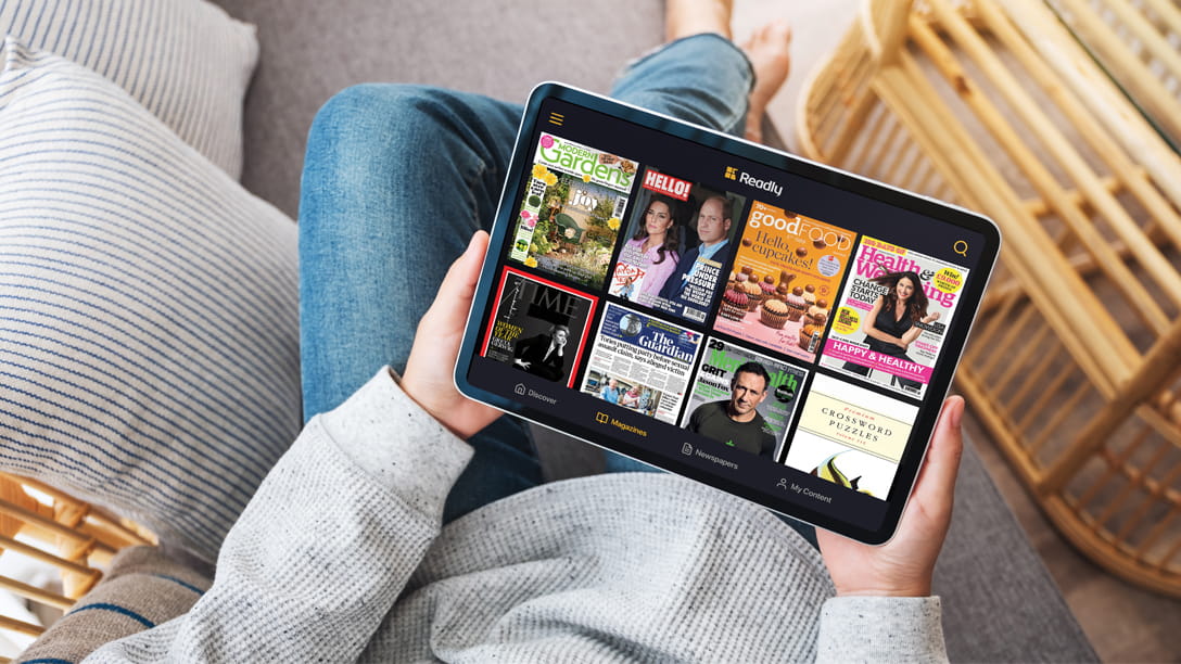 Person sitting on a sofa looking at magazine covers on a tablet