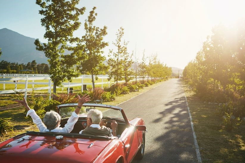 Man and woman in a convertible car with arms to the sky