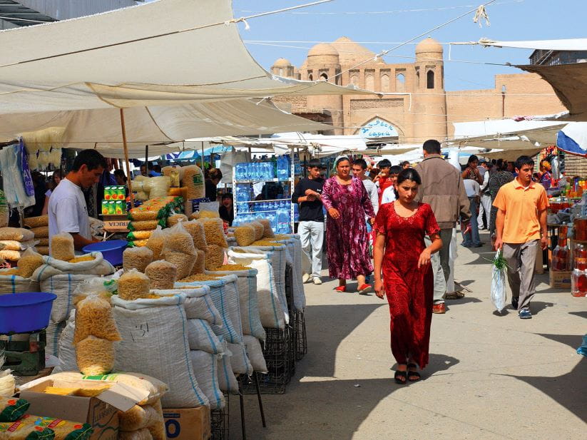Woman in red walking past market stalls with a town gate in the background
