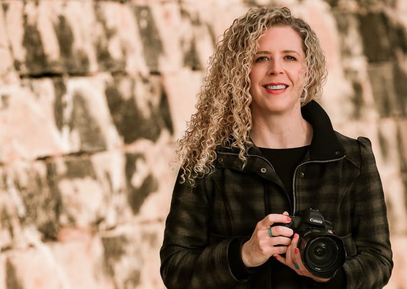 Bella Falk against a wall and holding her camera