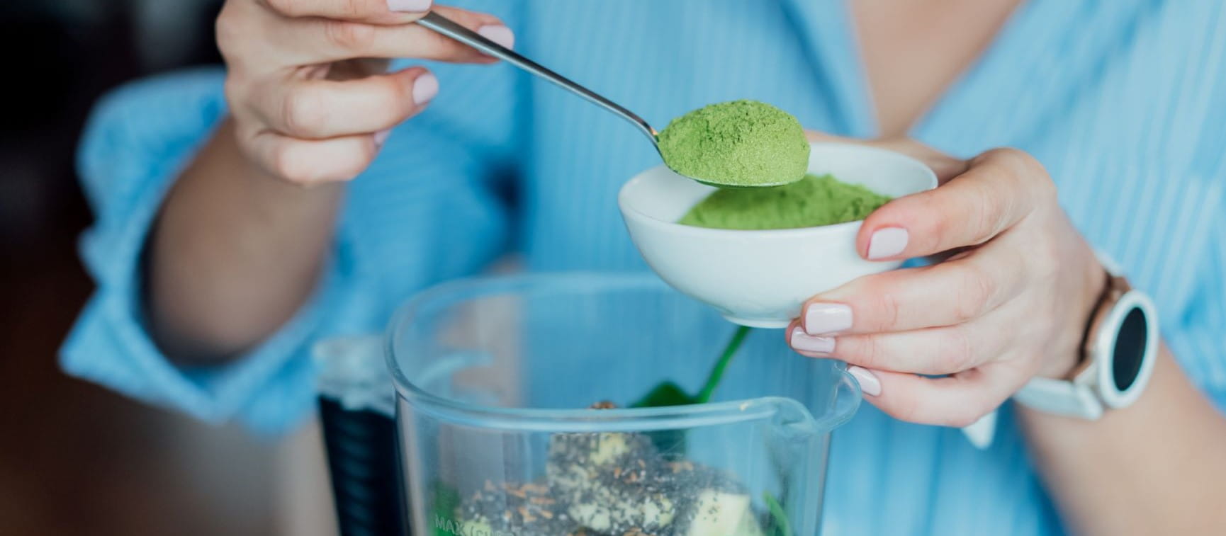 Close up woman adding wheat grass green powder during making smoothie on the kitchen. Superfood supplement.