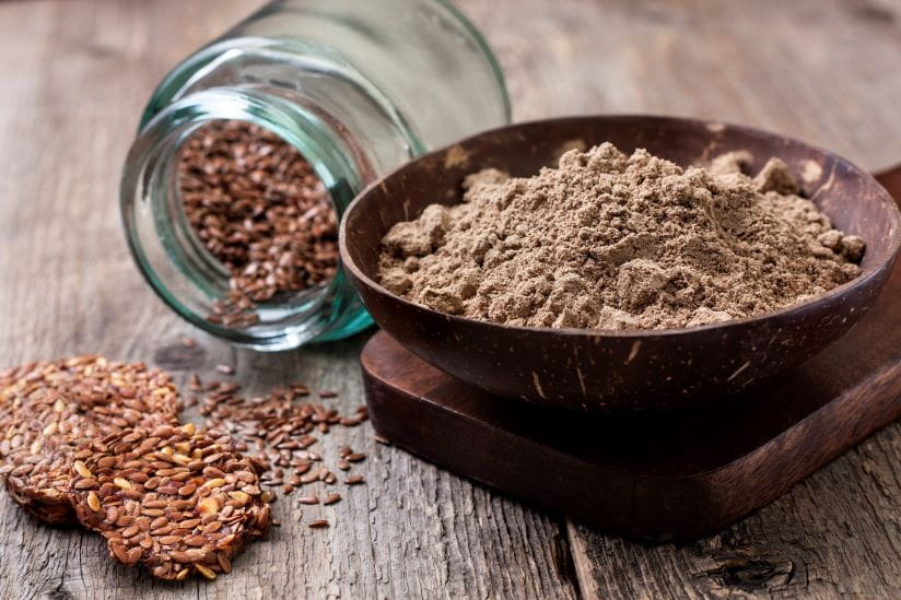 flax flour in a bowl, flax seed crackers, flax seeds in a glass jar on a wooden background