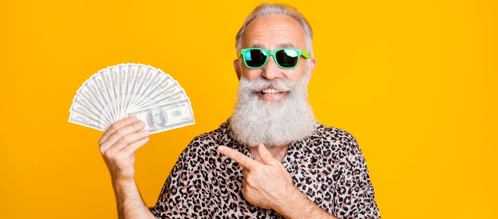 Man in sunglasses pointing to a fist fan of dollar notes against a white backdrop