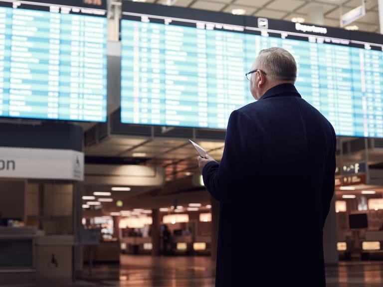 Man looking at the departures screen clutching his passport