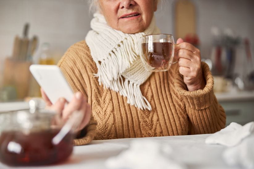 Lady keeping warm with a scarf, jumper and tea while checking her phone