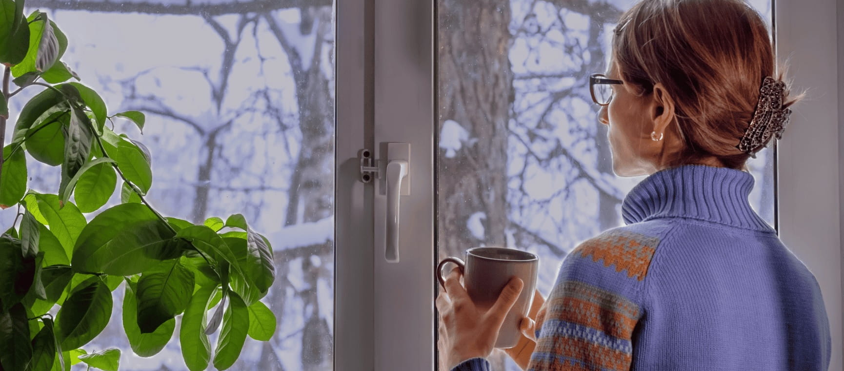 a woman drinking from a mug looking out at a snowy landscape