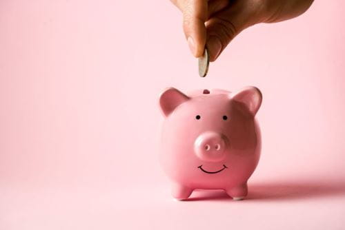Pink piggy bank with a pink background and a hand placing a coin in the slot