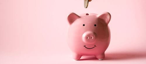 A coin being slotted into a pink piggybank
