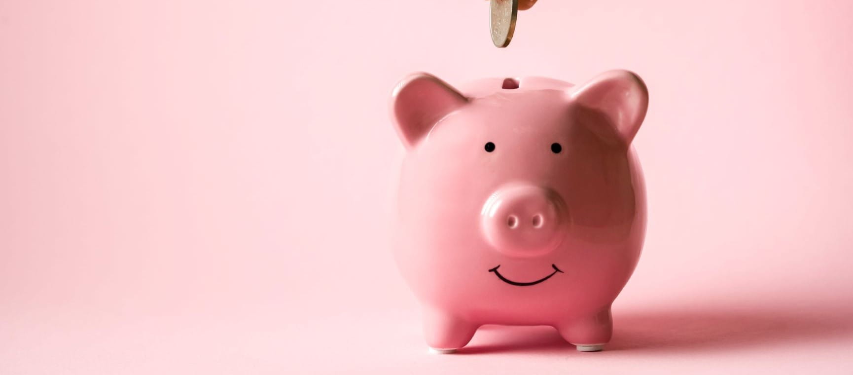 A coin being slotted into a pink piggybank