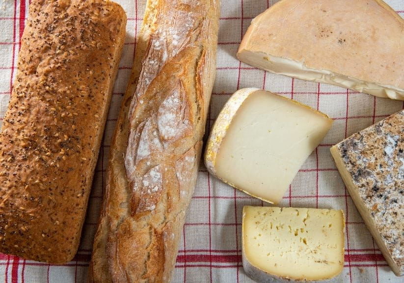 two loaves of bread and a selection of cheese on a checked tablecloth