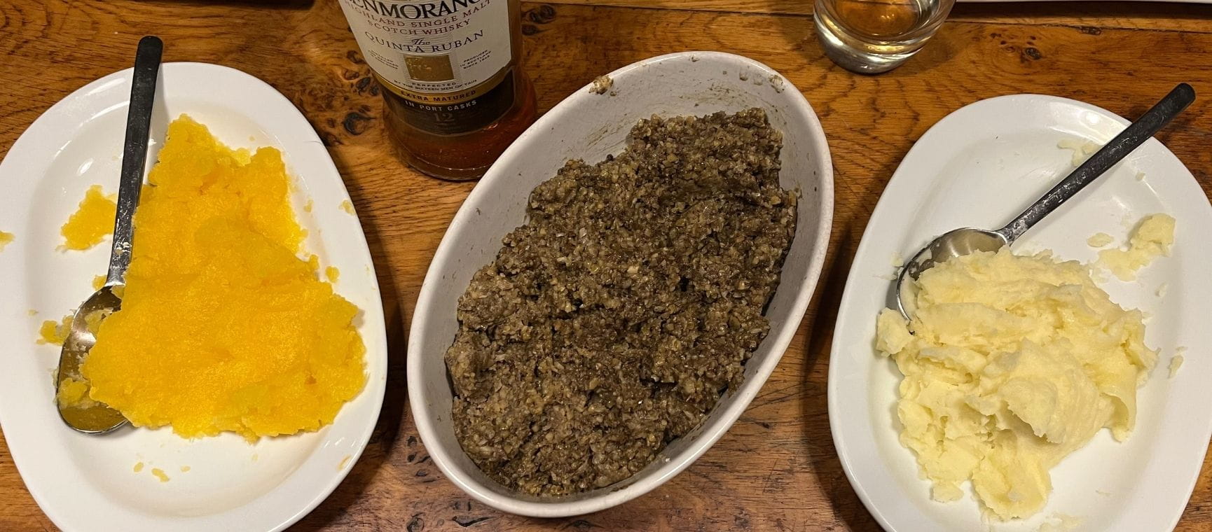A white dish of cooked haggis with traditional 'neeps and tatties' on a table top