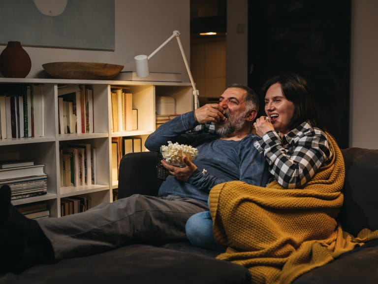 An older couple eating popcorn on a sofa at night