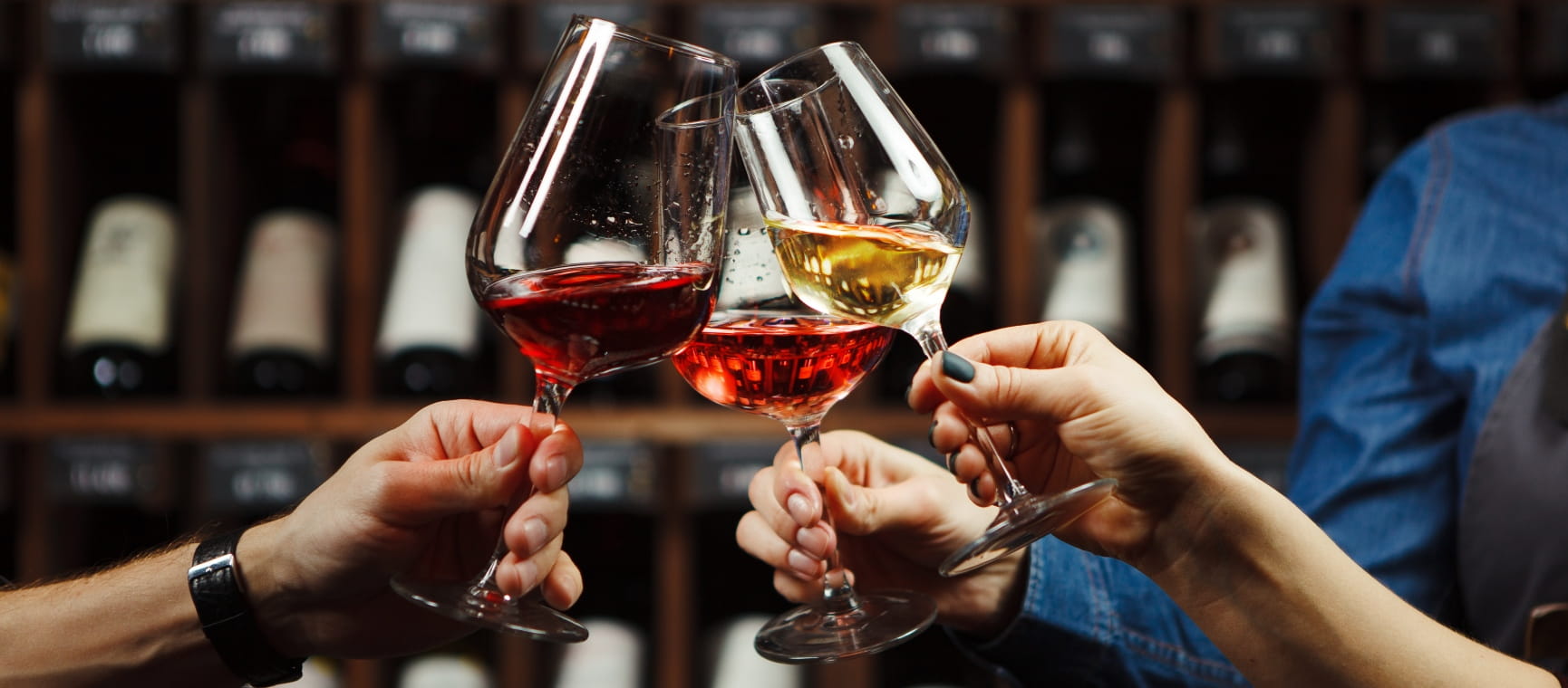 Three people clinking glasses of red and white wine in a wine cellar