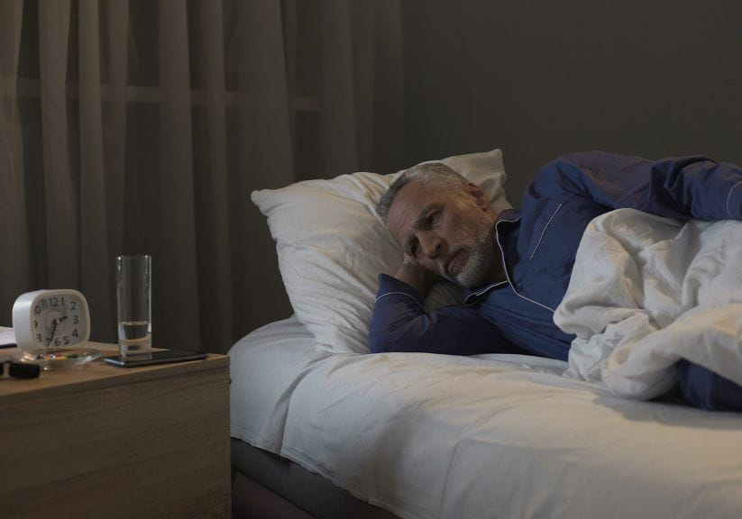 A man lies in bed looking at the clock as he struggles to go to sleep