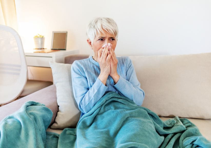 A mature woman blowing her nose with a cold