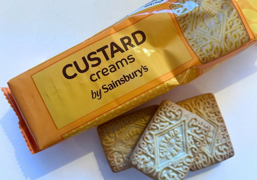 A shot of a packet of custard creams on a white background with two custard cream biscuits on the side
