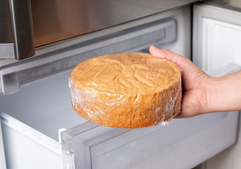 A person putting cake wrapped into clingfilm into a freezer drawer