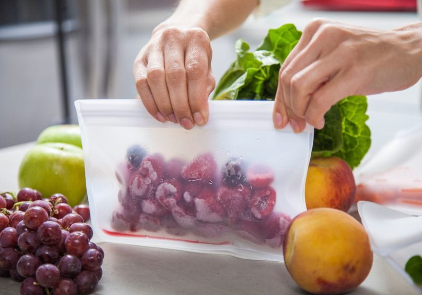 A woman sealing with a plastic bag containing frozen fruit in it