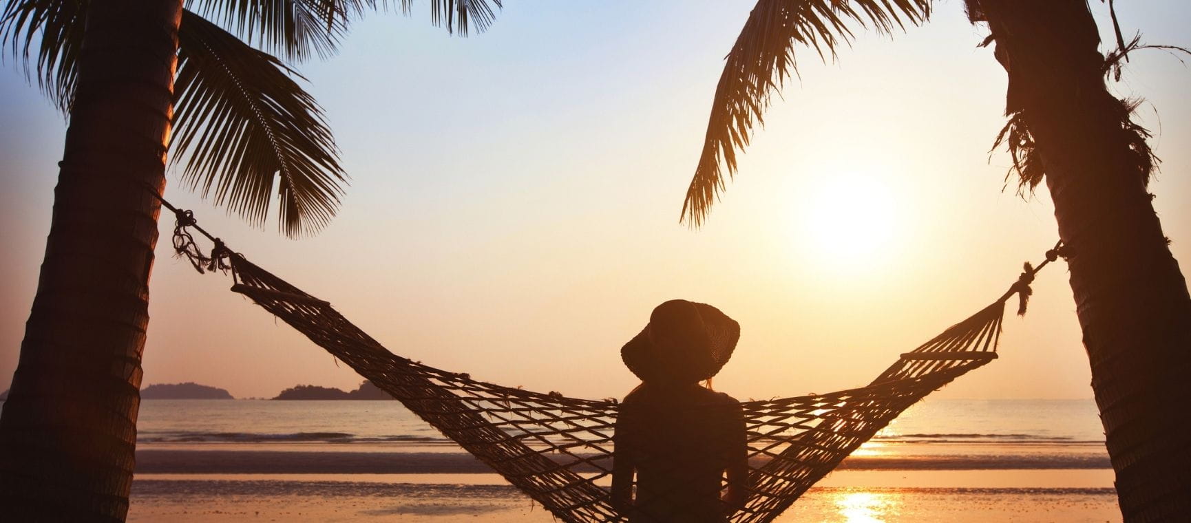 A woman sat in a hammock watching a sunset over the ocean